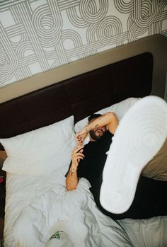 a man laying in bed with his feet up on the pillow and one hand over his face