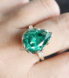 a woman's hand with a green ring on top of her finger and an emerald stone in the middle