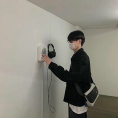 a person wearing a face mask and holding an electronic device in their hand while standing next to a wall