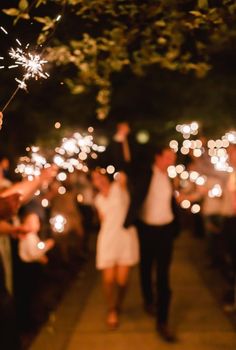 people holding sparklers in their hands and walking down the street with lights on them