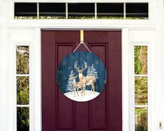 a red door with a white deer and pine trees painted on the front panel, hanging from a gold ribbon