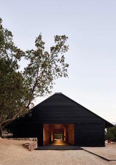 a black barn with an open door on the outside and trees in the front yard