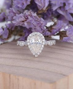 an engagement ring with a pear shaped diamond surrounded by purple flowers