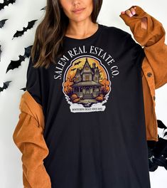 "👕MORE T-SHIRTS: tinyurl.com/SwagTshirts 👕MORE SWEATSHIRTS: tinyurl.com/SwagSweatshirts Welcome to the spooky world of real estate with our \"Salem Real Estate Co. Halloween Shirt\" - the perfect attire for all the realtors and real estate agents who dare to venture into the mysterious realm of property deals during the Halloween season! Product Details: - Design: Our exclusive shirt showcases a captivating blend of Halloween charm and professional pride. The front features a tastefully designed logo with \"Salem Real Estate Co.\" emblazoned in a hauntingly elegant font, surrounded by subtle ghostly silhouettes, witch hats, and bats. It's a delightful nod to the enchanting spirit of the season. - Material: Crafted from high-quality, breathable fabric, this shirt guarantees all-day comfor Salem Trip, Halloween Office Party, Spooky World, Real Estate Shirts, Witch Hats, Halloween Charms, Elegant Font, Unique Shirt, Real Estate Agents