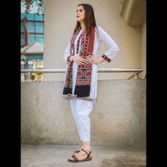 a woman standing in front of a building with her hands on her hips and wearing white pants