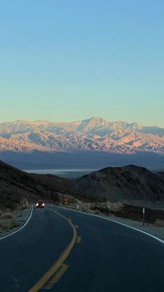 an empty road with mountains in the background and a car driving down it's side