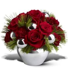 a white vase filled with red roses and greenery