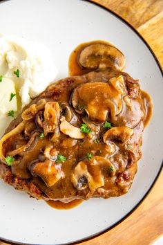 a white plate topped with meat covered in mushroom gravy and mashed potatoes