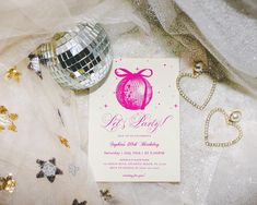 a pink and white birthday party card with disco ball on the table next to it