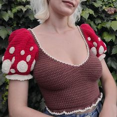 a woman with blonde hair wearing a red and white crochet top in front of bushes