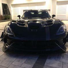 a black sports car parked in front of a garage with its hood up and lights on