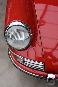 the front end of a red car with its lights turned on and headlight showing