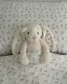 a white stuffed animal sitting on top of a bed covered in sheets and pillows with green leaves