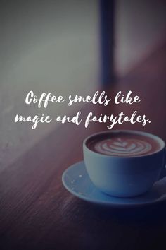 a cup of coffee sitting on top of a wooden table next to a quote about coffee smells like magic and fairy tales