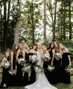 a group of women standing next to each other in front of trees and grass with bouquets