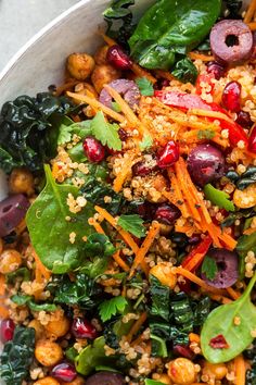 a salad with carrots, spinach and cranberries in a white bowl