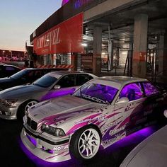 several cars parked in front of a building with purple lighting on the side of it