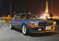 a mercedes benz parked in front of a gas station at night with the lights on