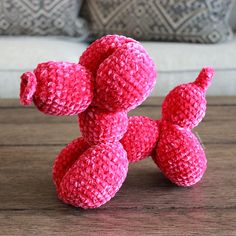 a pink crocheted teddy bear sitting on top of a wooden table next to pillows