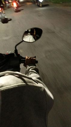 a person riding a motorcycle down a street at night with their reflection in the side mirror