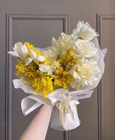 a hand holding a bouquet of flowers in front of a gray door with white and yellow flowers