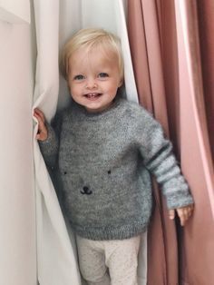 a little boy that is standing up against a curtain