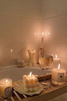 candles are sitting on a tray in front of a bathtub with a glass of wine