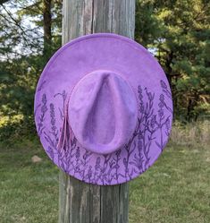 This truly one-of-a-kind hand burnt fedora is perfect to add a stylish flare to your outfit or hang as a unique floral wall decoration. The hat is a stunning shade of lilac that's sure to make any outfit stand out. It's burned entirely by hand using a pyrography tool with an original and entirely freehanded design (never using a stencil or laser machine.) The pastel purple faux suede material burns a gorgeous deep shade of purple. This design features lavender flowers growing up from the bottom Adjustable Western Purple Hat, Adjustable Lavender Wide Brim Hat, Lavender Adjustable Hat For Kentucky Derby, Adjustable Lavender Hat For Kentucky Derby, Adjustable Lavender Hat With Curved Brim, Adjustable Flat Brim Purple Felt Hat, Adjustable Purple Felt Hat With Flat Brim, Purple Adjustable Flat Brim Felt Hat, Adjustable Lavender Brimmed Hat