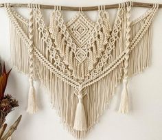 a crocheted wall hanging with tassels hangs on the wall next to a potted plant