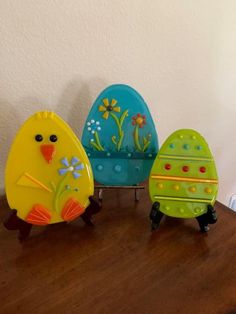 three plastic easter eggs sitting on top of a wooden table next to an egg holder