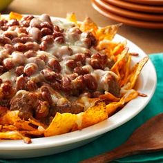 a white plate topped with chili and cheese covered nachos next to a green napkin