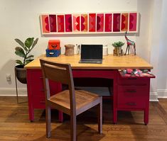 a desk with two chairs and a laptop on it in front of a wall mounted art piece