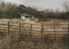 an old house sits in the distance behind a red fence that runs through a field