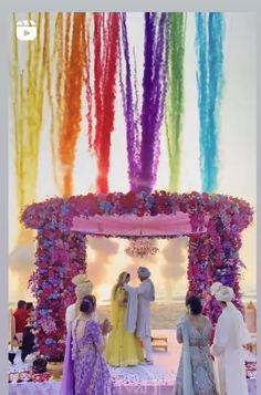 a group of people that are standing in front of a rainbow colored arch with flowers on it