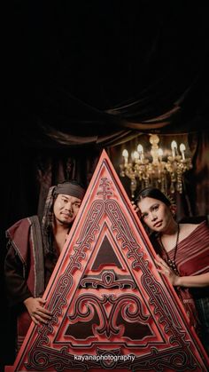 two people standing next to each other in front of a triangle shaped object with an intricate design on it