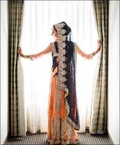 a woman standing in front of a window wearing an orange and blue dress with gold accents