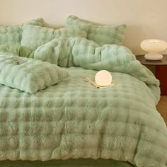 a bed with green comforter and pillows on it next to a night stand in a room