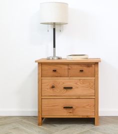 a wooden dresser with a lamp on top of it next to a white wall and floor