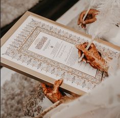 the wedding program is being held in an open book with feathers on it and two hands