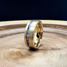 a wedding ring with two different colored stones on top of a wooden table in front of a black background