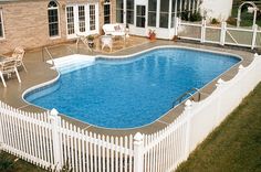 an above ground pool surrounded by a white picket fence and patio furniture with chairs around it