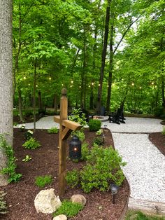 a wooden cross sitting in the middle of a garden next to a tree with lights on it