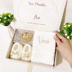 a person holding a box with baby shoes in it and some flowers on the table