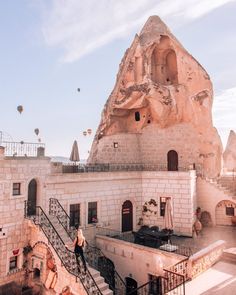 a woman walking up the stairs to a building with hot air balloons in the sky