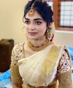 a woman in a white sari with gold jewelry on her neck and shoulders, posing for the camera