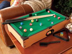 a pool table with cues and balls on it, next to a glass of wine