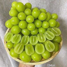 a person holding a wooden bowl filled with green grapes