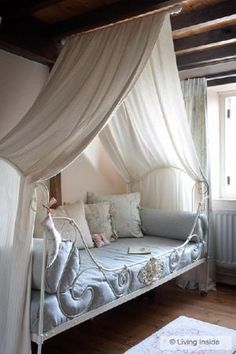 a canopy bed with white curtains and pillows