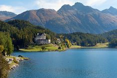 a house on the shore of a lake with mountains in the background