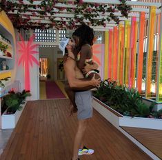 a man holding a baby in his arms while standing on a wooden floor next to flowers